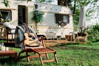 Wenn der Wohnwagen zum zweiten Zuhause wird: Die richtige Matratze fürs Dauercamping Ein fester Platz für die schönste Zeit Dauercamping erfreut sich in Deutschland schon seit einigen Jahren einer stetig wachsenden Beliebtheit: Anstatt jedes Jahr neue Ziele anzusteuern, sichern sich viele Familien einen festen Stellplatz auf einem Campingplatz und verbringen dort regelmäßig Wochenenden, Ferien oder sogar ganze Sommer. Der eigene Wohnwagen wird auf diese Weise zu einem zweiten, kleinen Zuhause, das ganzjährig fest an Ort und Stelle bleibt. Genau dieser dauerhafte Einsatz stellt allerdings andere Anforderungen an die Ausstattung als ein gelegentlicher Kurztrip, besonders wenn es um die passende Matratze für den festen Stellplatz geht. Andere Anforderungen als beim Kurztrip Während ein Wohnwagen, der nur wenige Wochenenden im Jahr genutzt wird, mit einer einfacheren Liegefläche auskommt, zeigt sich bei dauerhaftem Stellplatzbetrieb schnell ein anderes Bild. Der Wagen steht über Monate hinweg auf demselben Untergrund und ist Temperaturschwankungen zwischen kühlen Nächten und warmen Tagen ausgesetzt. Er wird insgesamt deutlich häufiger und intensiver genutzt als auf einer klassischen Rundreise mit dem Camper. Diese dauerhafte Beanspruchung stellt ganz besondere Ansprüche an Material, Belüftung und Langlebigkeit der eingesetzten Matratze. Feuchtigkeit als zentrales Thema Ein zentrales Thema beim Dauercamping ist die Feuchtigkeitsregulierung. Wohnwagen sind in der Regel deutlich schlechter isoliert als feste Gebäude, wodurch sich gerade an kühlen Tagen leichter Kondenswasser bilden kann, gerade an Stellen, an denen die Matratze direkten Kontakt zur Wand oder zum Boden hat. Eine hochwertige Wohnwagen Matratze mit atmungsaktivem, offenporigem Schaumstoff und einem robusten, gleichzeitig luftdurchlässigen Bezug beugt Schimmelbildung wirksam vor und sorgt dafür, dass die Liegefläche auch nach feuchten Nächten zügig wieder abtrocknet. Ungewöhnliche Grundrisse ausnutzen Auch die Größe verdient beim Dauercamping besondere Aufmerksamkeit, denn Wohnwagen bringen oft ungewöhnliche Grundrisse mit sich. Abgeschrägte Ecken am Bug, integrierte Staufächer unter der Liegefläche oder asymmetrische Betten sind alles andere als selten und lassen sich mit reinen Standardmaßen aus dem Möbelhaus nur selten wirklich zufriedenstellend lösen. Eine passgenau nach den eigenen Maßen gefertigte Lösung schließt solche Lücken vollständig, was nicht nur den Schlafkomfort spürbar erhöht, sondern auch zuverlässig verhindert, dass Kleinteile oder Zubehör in schwer erreichbaren Zwischenräumen verschwinden. Langlebigkeit über viele Saisons Da der Wohnwagen beim Dauercamping oft über Jahre am gleichen Platz steht, lohnt sich außerdem der Blick auf die Langlebigkeit der verwendeten Materialien. Ein hochwertiger Kaltschaum mit ausreichender Rohdichte behält seine stützende Wirkung zuverlässig auch nach jahrelanger, regelmäßiger Nutzung, während deutlich günstigere Schaumstoffe spürbar schneller durchliegen und mit der Zeit an Komfort verlieren. Wer über mehrere Saisons hinweg gut schlafen möchte, sollte deshalb nicht am Material sparen, sondern gezielt in eine Ausführung investieren, die für den Dauereinsatz gemacht ist. Der passende Härtegrad für zwei Auch der individuelle Härtegrad bleibt beim stationären Wohnwagen ein wichtiges Thema, denn anders als bei einer kurzen Reise wird hier über viele Wochen im Jahr geschlafen. Wer zu zweit auf dem eigenen Stellplatz lebt, profitiert spürbar davon, den Härtegrad individuell an das eigene Körpergewicht anzupassen oder sogar zwei unterschiedliche Zonen in einer einzigen Matratze zu kombinieren, damit beide Partner gleichermaßen gut schlafen, ganz unabhängig von individuellen Vorlieben, Gewicht und persönlichen Bedürfnissen. Ein echtes Zuhause auf Zeit Wer all diese Punkte beim Kauf sorgfältig berücksichtigt, sichert sich langfristigen und verlässlichen Schlafkomfort auf dem eigenen Stellplatz, Saison für Saison aufs Neue. Eine durchdacht ausgewählte Matratze macht den Unterschied zwischen einem Wohnwagen, der sich wie ein bloßes Provisorium anfühlt, und einem echten zweiten Zuhause. In diesem kann sich die ganze Familie Saison für Saison über Jahre hinweg richtig wohlfühlen.